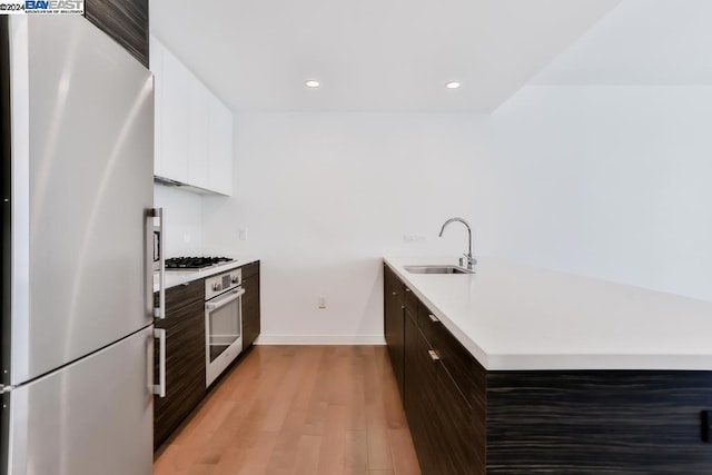 kitchen featuring sink, light wood-type flooring, appliances with stainless steel finishes, dark brown cabinets, and white cabinetry