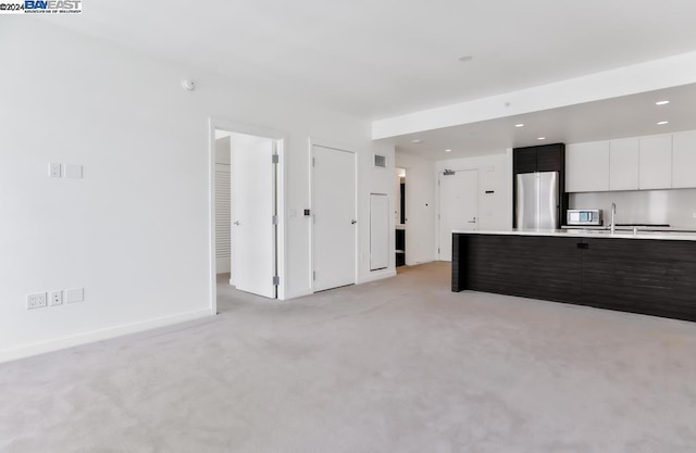 unfurnished living room featuring sink and light carpet