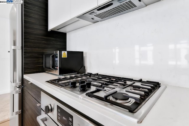 room details featuring extractor fan, backsplash, stainless steel appliances, and white cabinetry