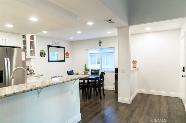 kitchen with dark hardwood / wood-style floors, stainless steel fridge with ice dispenser, light stone counters, and white cabinets