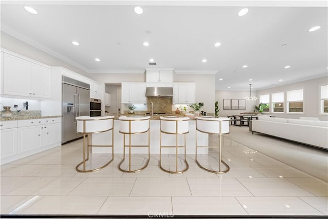 kitchen with a kitchen breakfast bar, wall chimney exhaust hood, stainless steel built in refrigerator, white cabinets, and an island with sink