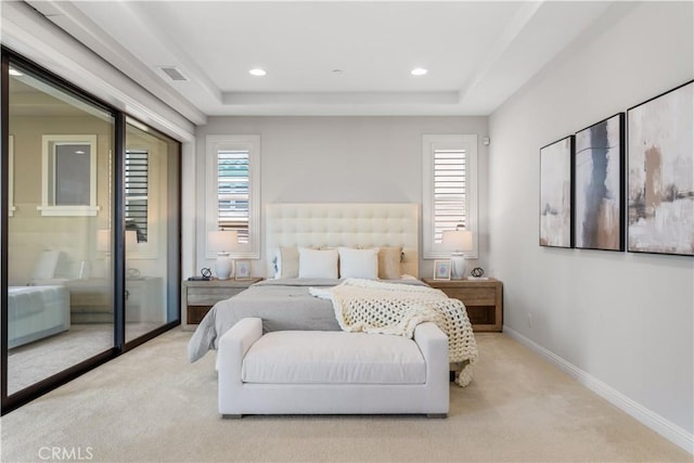 bedroom with light carpet, a tray ceiling, and multiple windows