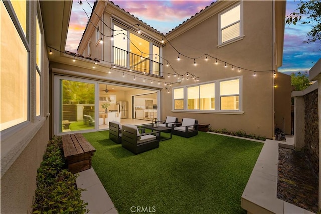 back house at dusk featuring an outdoor hangout area, a balcony, a patio, and a lawn