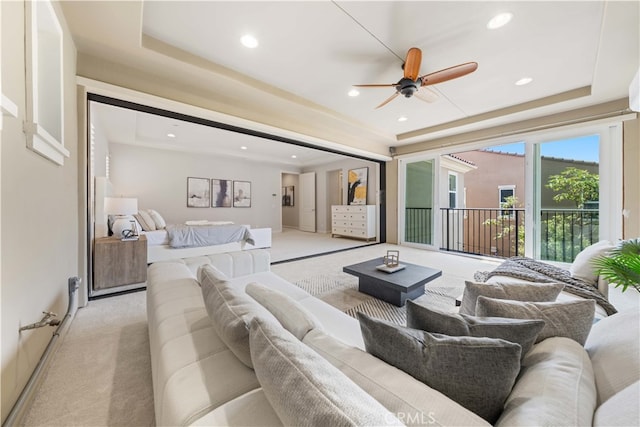 carpeted living room with a raised ceiling and ceiling fan