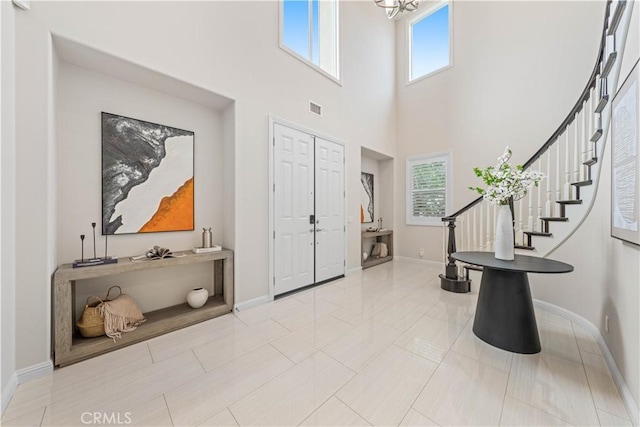 entrance foyer with light tile patterned floors, a towering ceiling, an inviting chandelier, and a wealth of natural light