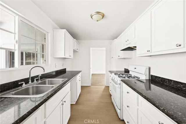 kitchen featuring light wood-type flooring, white cabinets, dark stone counters, sink, and white range with gas stovetop