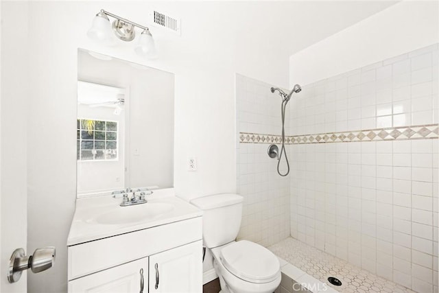 bathroom featuring tiled shower, ceiling fan, vanity, and toilet