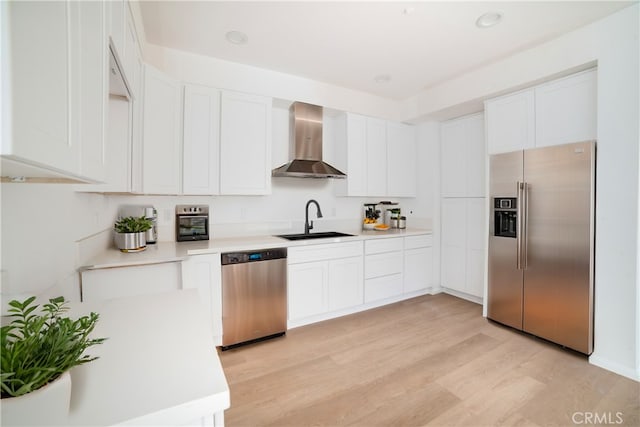 kitchen featuring light hardwood / wood-style floors, white cabinets, wall chimney exhaust hood, stainless steel appliances, and sink