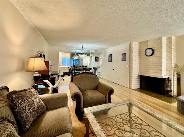 living room with wood-type flooring, a textured ceiling, a brick fireplace, and ornamental molding