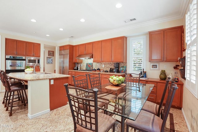 kitchen featuring a center island with sink, sink, built in appliances, and crown molding