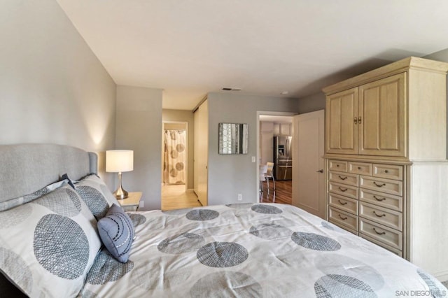 bedroom with wood-type flooring, stainless steel refrigerator with ice dispenser, and ensuite bathroom