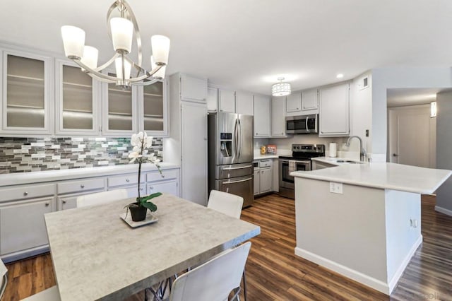 kitchen with sink, kitchen peninsula, decorative light fixtures, dark wood-type flooring, and appliances with stainless steel finishes