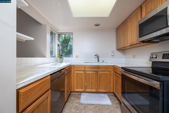 kitchen with appliances with stainless steel finishes, kitchen peninsula, tile counters, and sink