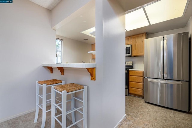 kitchen with kitchen peninsula, tile counters, a breakfast bar area, and stainless steel appliances