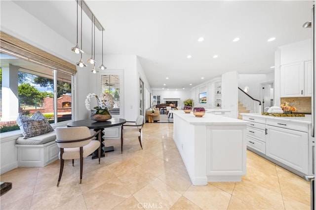 kitchen featuring a center island, tasteful backsplash, decorative light fixtures, light tile patterned flooring, and white cabinetry