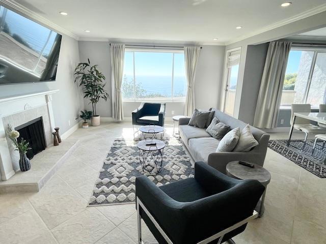 living room with crown molding, a water view, and a high end fireplace