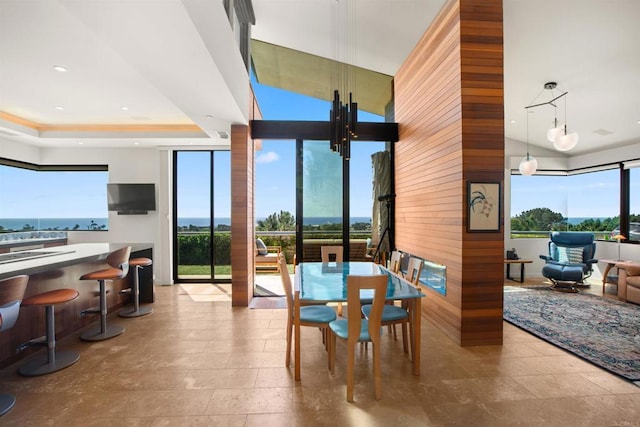 dining space with plenty of natural light, a high ceiling, wooden walls, and a tray ceiling