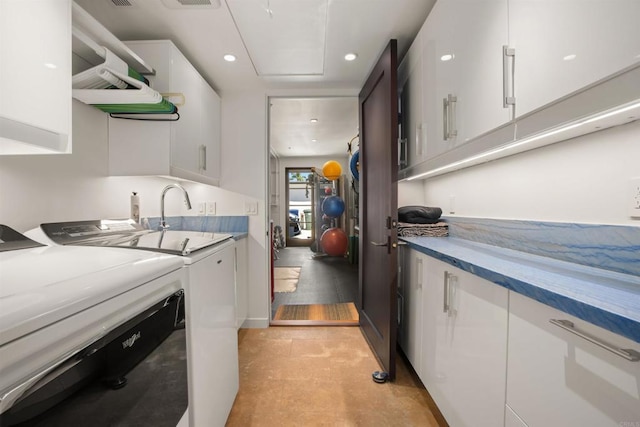 laundry area featuring washing machine and dryer, sink, light tile patterned floors, and cabinets