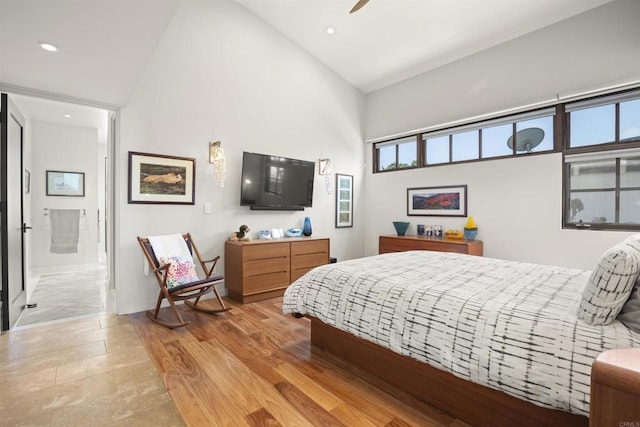 bedroom with multiple windows, ensuite bathroom, light hardwood / wood-style flooring, and high vaulted ceiling