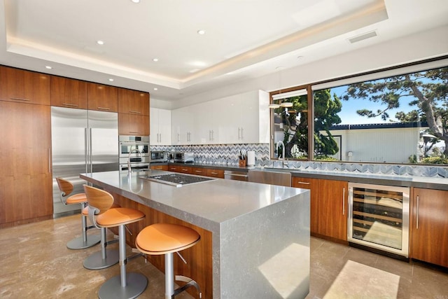 kitchen with sink, a raised ceiling, wine cooler, white cabinets, and appliances with stainless steel finishes