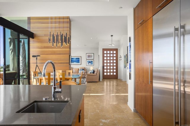 kitchen with built in fridge, sink, wood walls, and decorative light fixtures