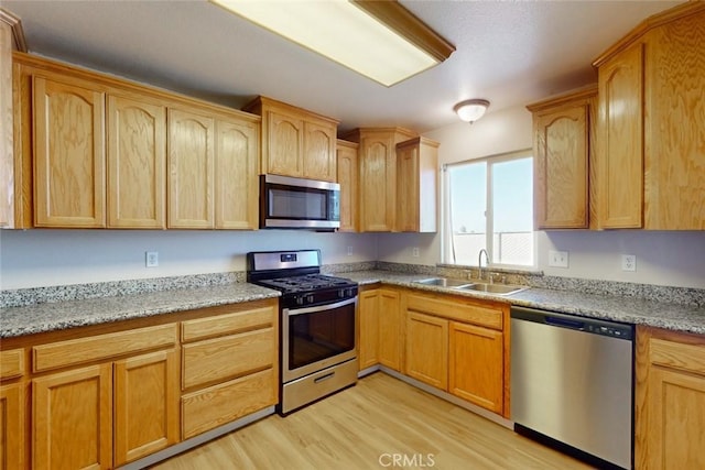 kitchen with light wood-type flooring, light stone countertops, stainless steel appliances, and sink