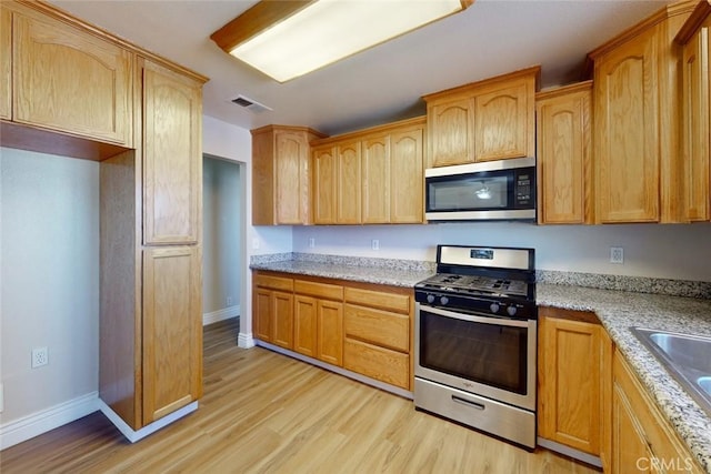 kitchen featuring light stone countertops, appliances with stainless steel finishes, sink, and light hardwood / wood-style floors