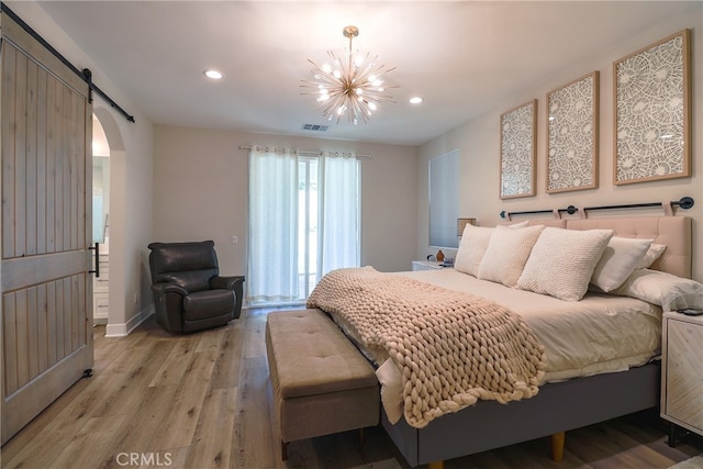 bedroom with a notable chandelier, light wood-type flooring, and a barn door