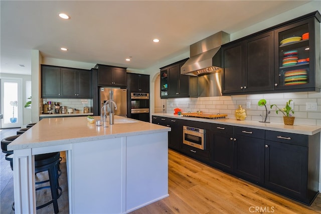 kitchen featuring decorative backsplash, stainless steel appliances, light wood-type flooring, a center island with sink, and sink