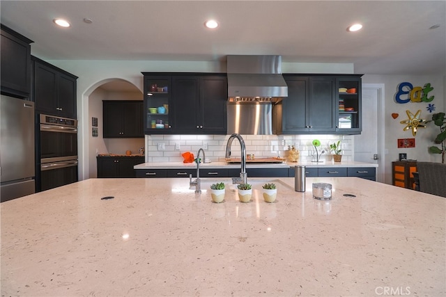 kitchen featuring light stone countertops, stainless steel appliances, wall chimney exhaust hood, and decorative backsplash