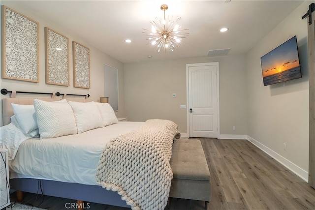 bedroom featuring a barn door, wood-type flooring, and a chandelier