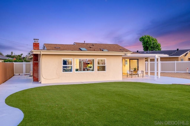 back house at dusk with a patio area and a yard