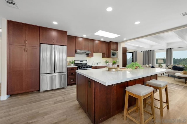 kitchen featuring appliances with stainless steel finishes, a breakfast bar, beamed ceiling, light hardwood / wood-style flooring, and a skylight