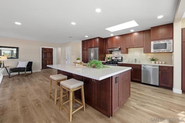 kitchen featuring a skylight, sink, light hardwood / wood-style flooring, appliances with stainless steel finishes, and a breakfast bar