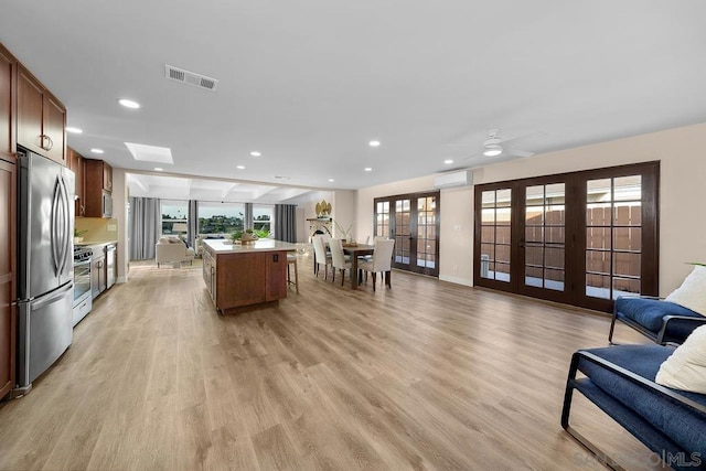 living room with ceiling fan, light wood-type flooring, a wall mounted air conditioner, and a wealth of natural light