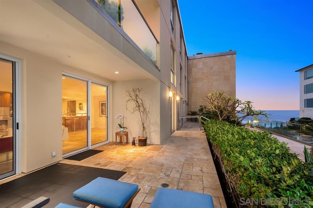 patio terrace at dusk featuring a balcony and a water view