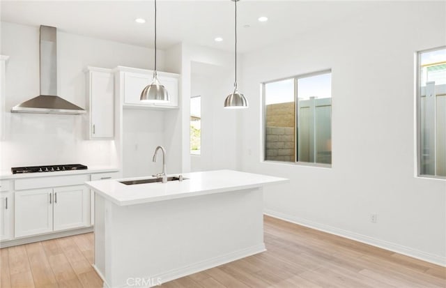 kitchen with a center island with sink, sink, wall chimney range hood, and white cabinets