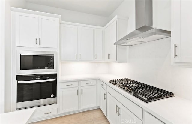 kitchen with stainless steel appliances, white cabinetry, light wood-type flooring, and wall chimney exhaust hood