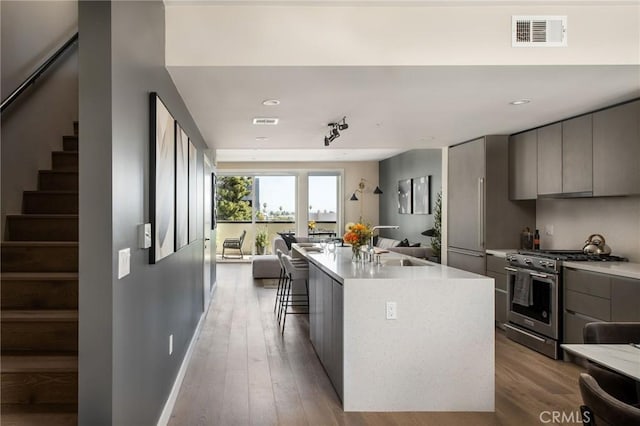 kitchen featuring high end stove, gray cabinets, an island with sink, and light wood-type flooring