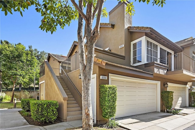 view of front of property featuring stairway, an attached garage, a chimney, stucco siding, and concrete driveway