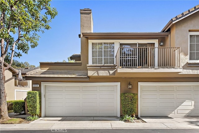 multi unit property featuring stucco siding, driveway, a garage, a balcony, and a tiled roof