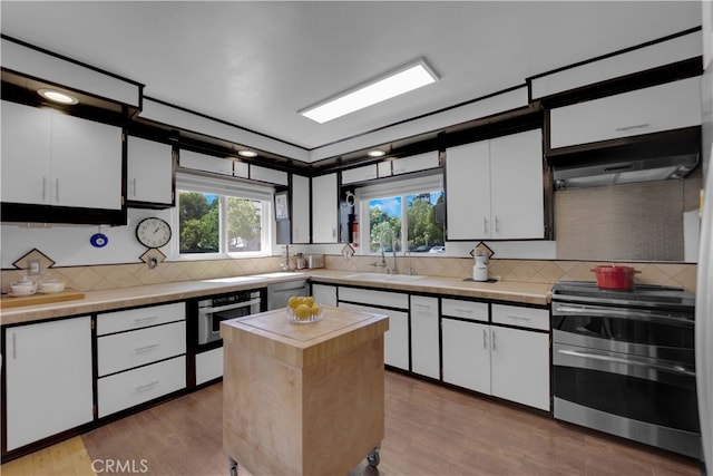 kitchen featuring appliances with stainless steel finishes, tasteful backsplash, white cabinets, light hardwood / wood-style flooring, and sink