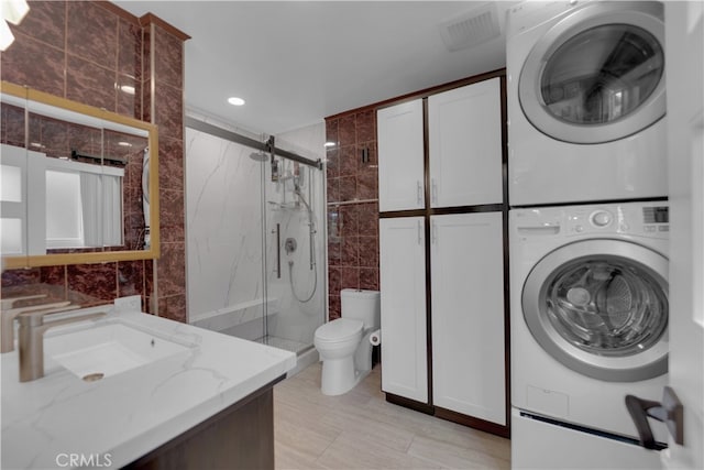 washroom with sink, tile walls, a barn door, and stacked washer and dryer