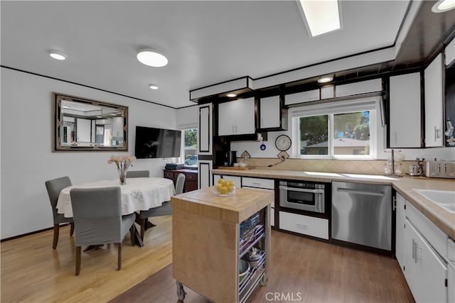 kitchen featuring appliances with stainless steel finishes, wood-type flooring, white cabinetry, and decorative backsplash