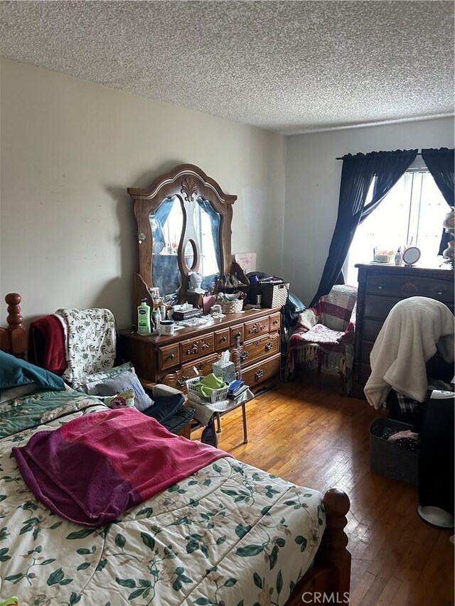 bedroom with a textured ceiling, hardwood / wood-style flooring, and multiple windows