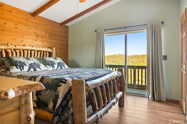 bedroom featuring access to outside, wood-type flooring, lofted ceiling with beams, a mountain view, and wood walls