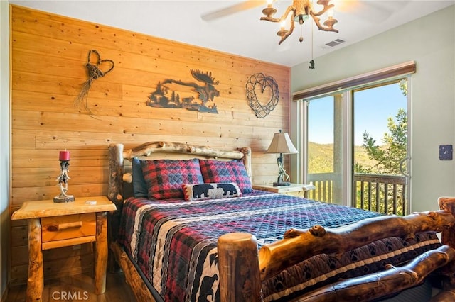 bedroom featuring access to exterior, ceiling fan, wooden walls, and hardwood / wood-style floors