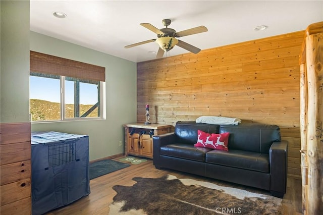 living room with ceiling fan, wood walls, and wood-type flooring