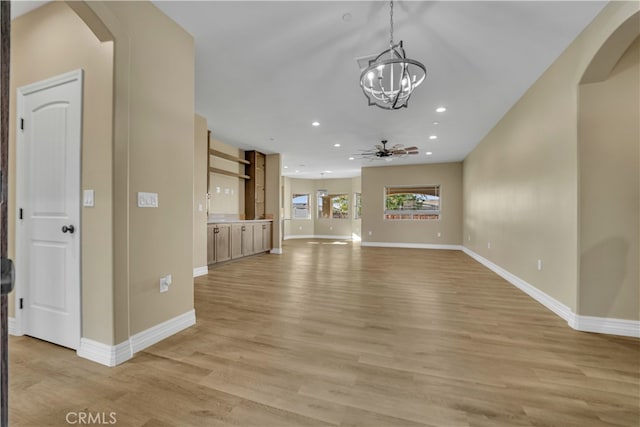 unfurnished living room with ceiling fan with notable chandelier and light hardwood / wood-style flooring