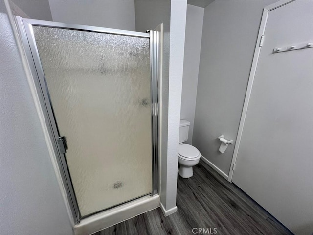 bathroom featuring wood-type flooring, toilet, and a shower with door